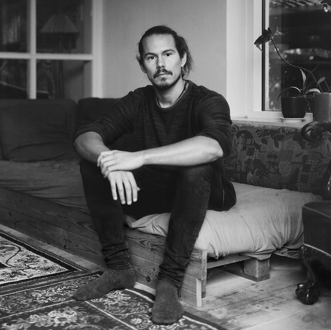 black and white photo of person sitting on sofa in a living room looking directly into the camera