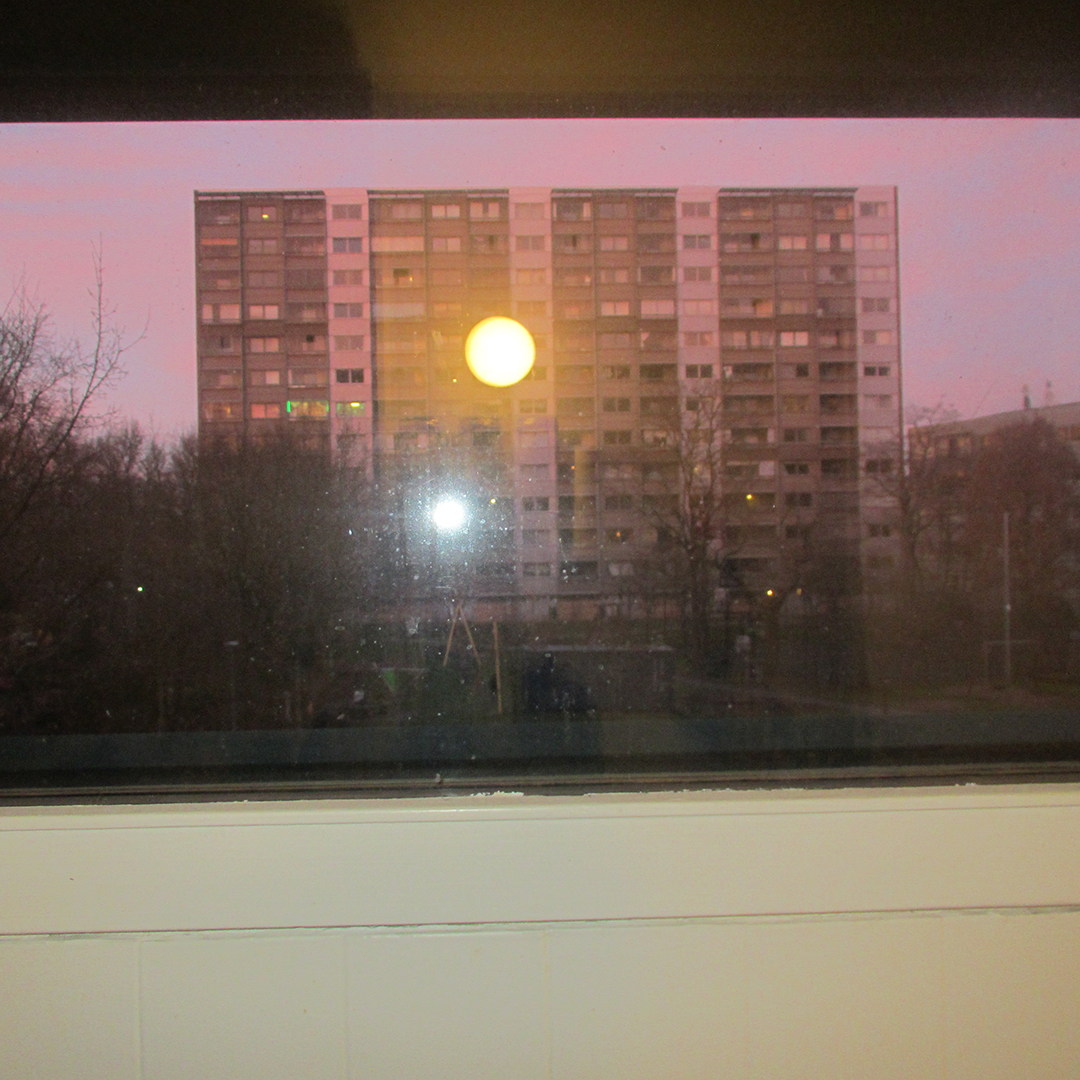 photo of block building with pink sky from sunset seen from window - reflection of light and flash visible in window
